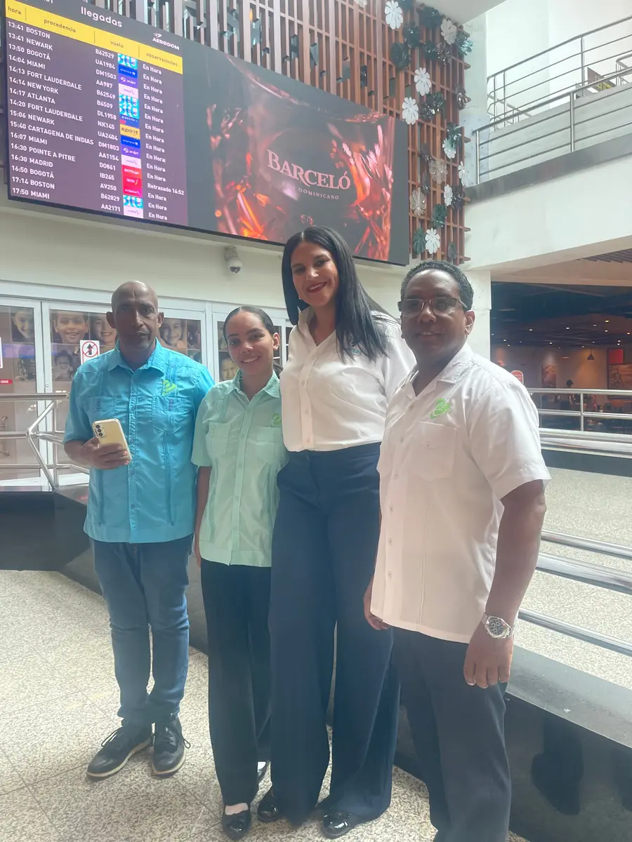 Equipo de eTransferSDQ en la sala de llegadas del aeropuerto Las Américas, bajo la pantalla de llegadas